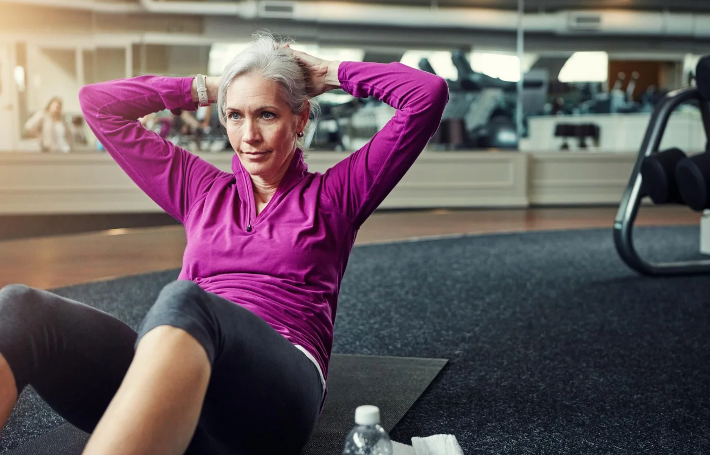Mature woman doing sit-ups on a mat at the gym, wearing activewear.