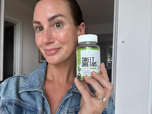 Woman holding an Organic Innovation Sweet Dreams Organic Melatonin Gummy Bear Bottle and Smiling At the Camera