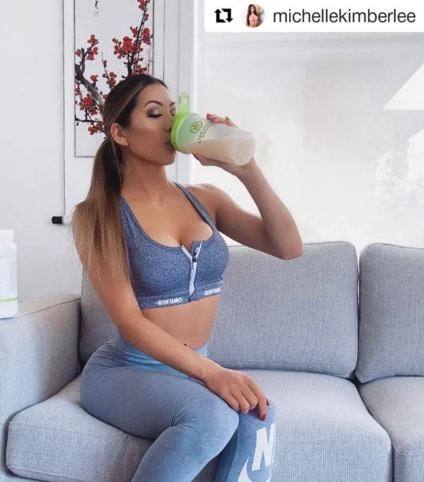 Woman in athletic wear drinking from a shaker bottle while sitting on a couch.