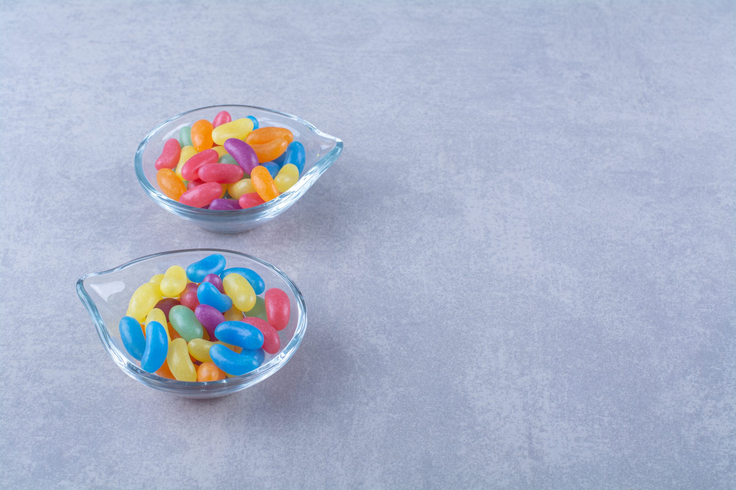Two glass plates with fruit sweet bean candies on blue-gray background